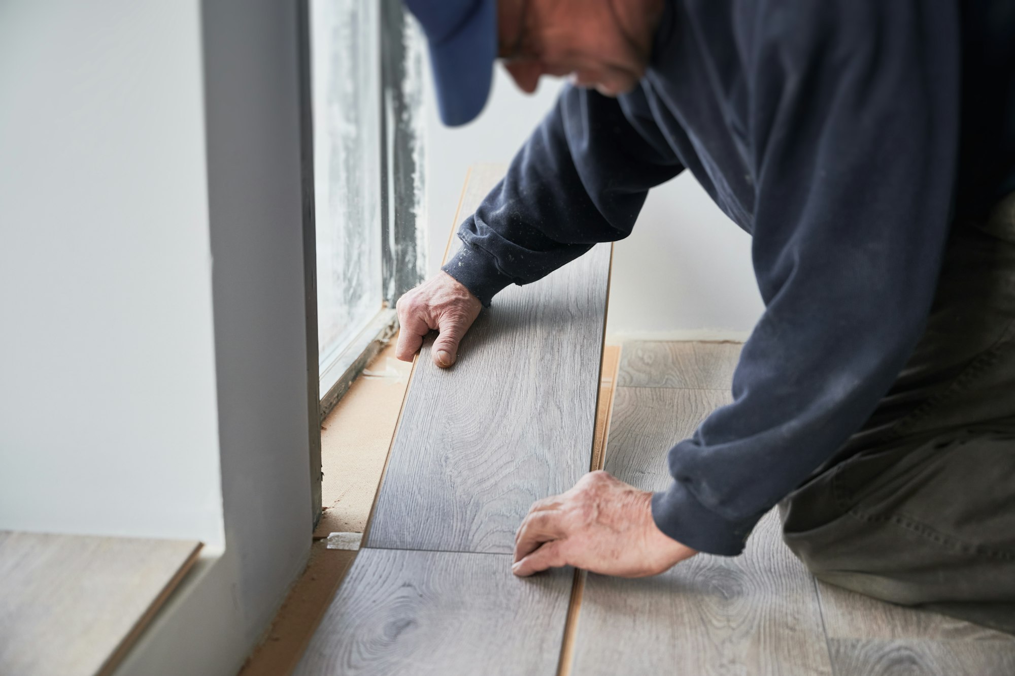 Man installing laminate floor in apartment under renovation.